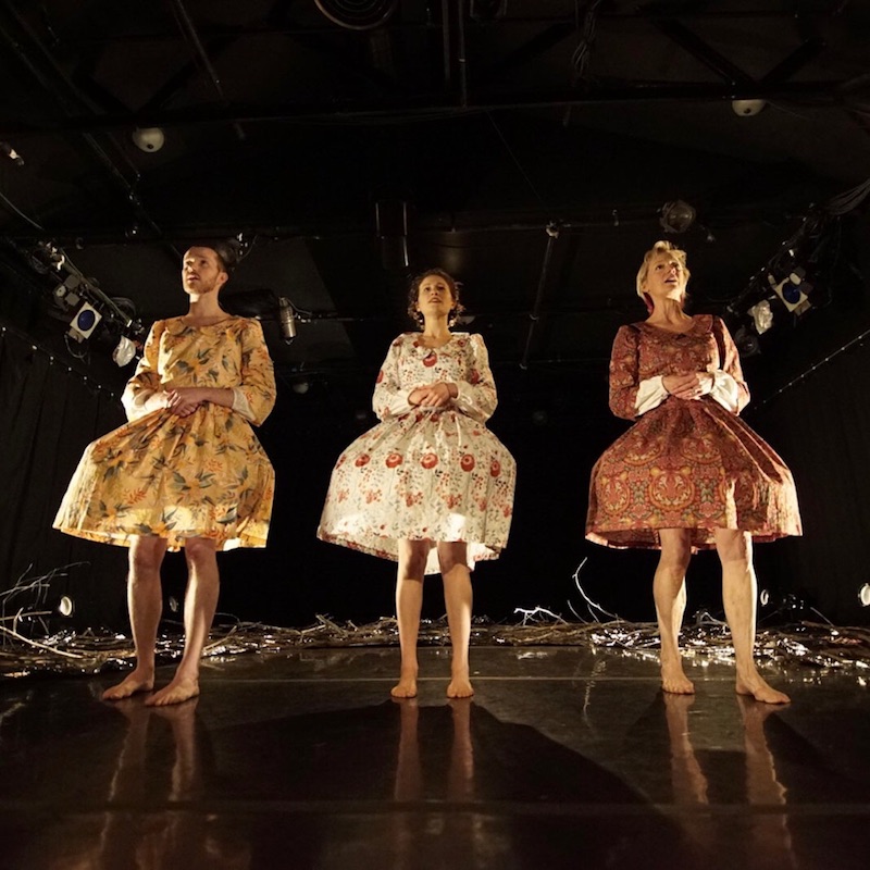 The three artists stand in front of the mylar and branch set in floral blouses and skirts
